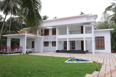 a white house with a palm tree and a yard at Village Pavilion in Tellicherry