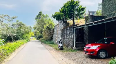 a red car parked next to a wall next to a road at White Fort Holiday Home in Vythiri