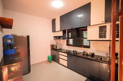 a kitchen with black and white cabinets and a refrigerator at Wayanadan Huts Homestay in Sultan Bathery