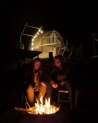 two women sitting around a fire pit at night at Cocoon-coxcargill in Vattavada