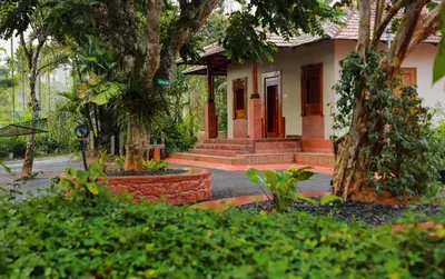 a house with a tree and some bushes at Kudajadri Drizzle Homestay in Kaniyāmbetta