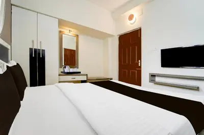 a bedroom with a white bed and a flat screen tv at Hotel O Ondipudur Bus Terminal Formerly New Paradise Inn in Irugūr