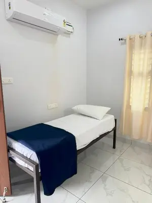 a small bed with a blue blanket on it in a room at Joseph's Residency Homestay in Podanūr