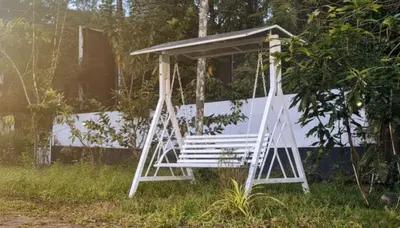 a white porch swing sitting in the grass at Forest Soul by BOB Hotels - Forest Retreat with Pool in Batheri