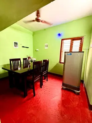 a dining room with a table and a refrigerator at GSC Family Cottage in Samattūr