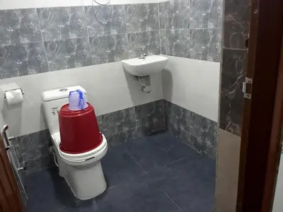 a bathroom with a toilet with a sink and a red cooler at Benzy Tourist Home in Ponnāni