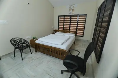 a bedroom with a bed and two chairs and a window at Tranquil Rest House in Trichūr