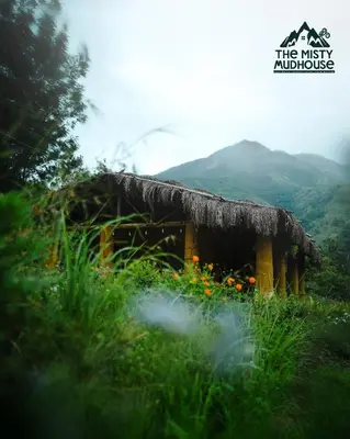 a cabin in a field of grass with mountains in the background at The Misty Mudhouse in Marayoor