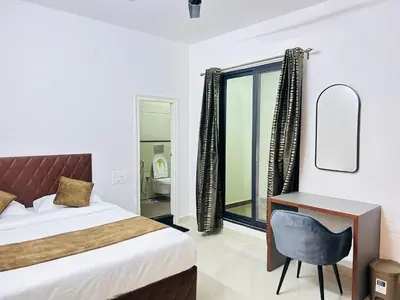 a bedroom with a bed and a desk and a window at Queens Suite Rooms in Channapatna