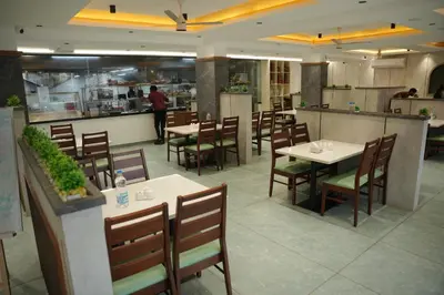 a restaurant with tables and chairs and a person in the kitchen at Denz Paradise in Kelakam
