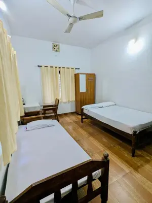 a room with two beds and a ceiling fan at Gods Gift Homestay James Inn in Kozhikode