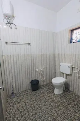 a bathroom with a toilet and a tile floor at Gods Gift Homestay James Inn in Kozhikode