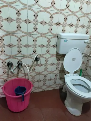 a bathroom with a toilet and a pink bucket at Laali Dormitory in Madikeri