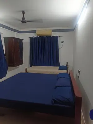 a bedroom with two beds and a blue curtain at Poonthanam guest house in Guruvāyūr