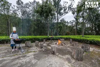 a man standing next to a grill and a fire at StayVista at Sande's Farview with Bonfire in Coonoor