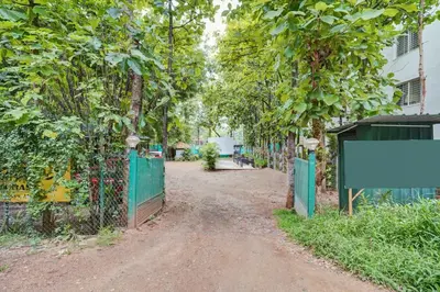 a dirt road with a green fence and trees at Collection O Mysore Shri Lakshmikantha Swamy Temple in Mysore