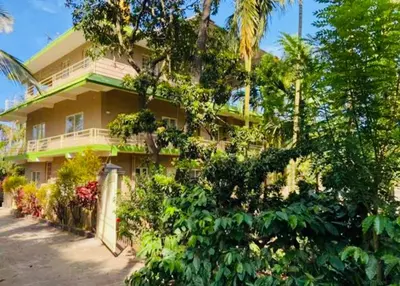 a yellow house with trees and flowers in front of it at Safari Inn in Kurchi