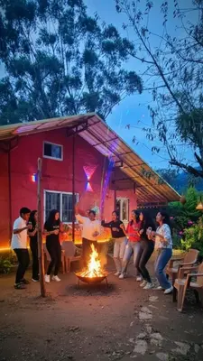 a group of people standing around a fire in front of a house at Madama Mudhouse Edenwood Retreats in Kanthalloor