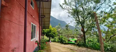 a red building with a tree and a mountain in the background at Madama Mudhouse Edenwood Retreats in Kanthalloor