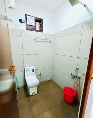 a small bathroom with a toilet and a red bucket at Chembani Holidays and Resorts Kanthalloor in Kanthalloor