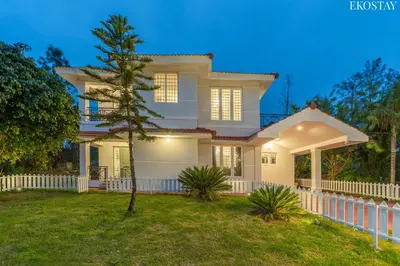 a white house with a fence and a tree at EKOSTAY - Villa Eve in Ooty