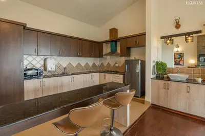 a large kitchen with wooden cabinets and chairs in it at EKOSTAY - Skyfall Dew Drops in Ooty