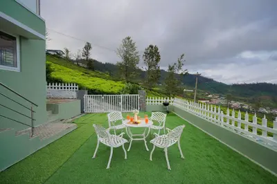 a patio with a table and chairs on the grass at EKOSTAY - Dutch Cottage in Ooty
