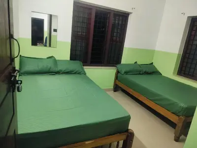 two beds in a room with green walls and windows at Clap House Home in Guruvāyūr