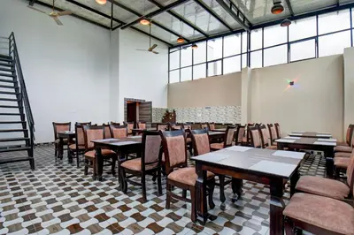 a dining room with tables and chairs and windows at Super Townhouse Oak Sri Mahadeshwara Convention Centre Formerly Shri Aprameya Resort in Mysore