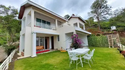 a white house with a table and chairs in the yard at Mayfield Valley Homestay in Kotagiri
