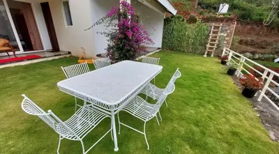 a white table and chairs on a lawn with flowers at Mayfield Valley Homestay in Kotagiri