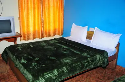 a bed with white pillows and a television in a room at Hotel Zaraa in Ooty