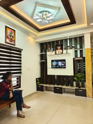 a woman sitting on a bench in a room with a tv at Full Home Wayanad Bathery in Sultan Bathery