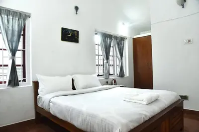 a bedroom with a large white bed with two windows at Mountain Villa Ooty Rooms in Ooty