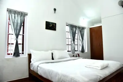 a bedroom with a white bed with two windows at Mountain Villa Ooty Rooms in Ooty