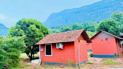 a red house with a mountain in the background at Jungle Homes in Kollengode
