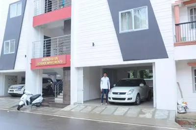 a man standing in front of a building with a car at Brindavan Service Apartments in Mysore