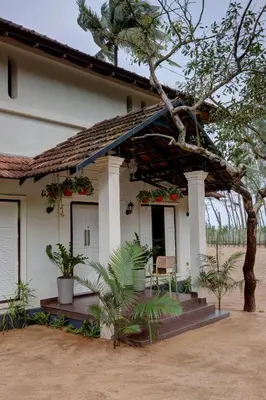 a small white house with a porch and a tree at Bougainvillea Beach Home - Guruvayur - Chavakkad in Manattala