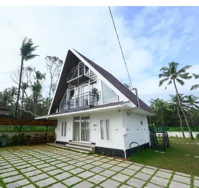 a white house with a black roof at Heaven-Vadanapilly Beach Villa in Irimbranallūr