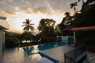 a swimming pool on a house with the sunset in the background at Lake Paradise Resort in Padinjarathara