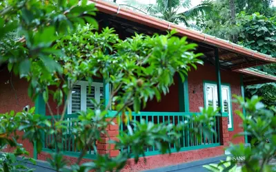 a red house with a blue balcony and trees at Paddy Land in Wayanad