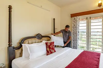 a man standing next to a bed in a bedroom at Mihirika's Nirvana 5-BHK With Garden, Gazebo, Bonfire Pit & Scenic Views in Ooty
