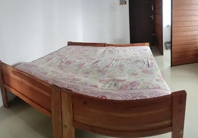 a wooden bed in a room with a mattress at Aswathy Bhavan Vadakkenchery Near Star auditorium in Vadakkāncheri