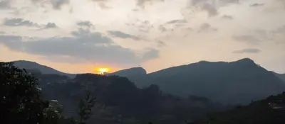 a sunset over a mountain range with the sun in the sky at Misty plaza in Munnar