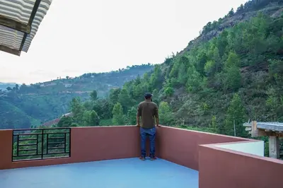 a man standing on a ledge looking at a mountain at Climate Dull - Homestay Villa in Ketti