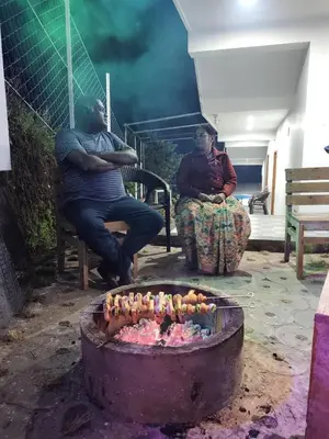 two men sitting on benches next to a fire at diamond hill view cottage in Ooty