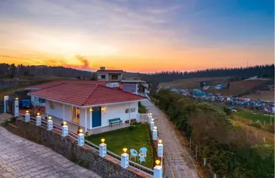 a house with a red roof with a sunset in the background at The Lake House Ooty in Ooty