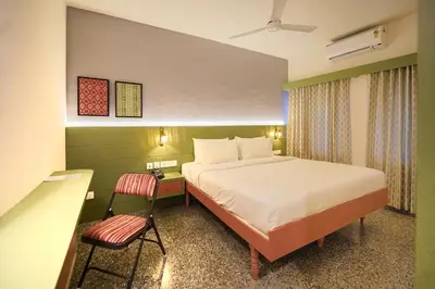 a hotel room with a bed and a chair at Sreenivas Lodge by Copperfolia in Kozhikode