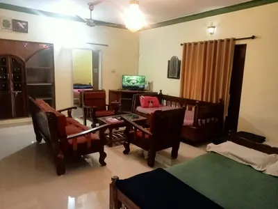 a living room with a bed and chairs and a television at Somanna Estate stay in Madikeri