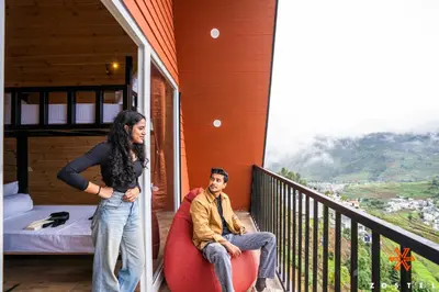 a woman standing on a balcony with a man in a chair at Zostel Kodaikanal, Vilpatti in Kodaikānāl